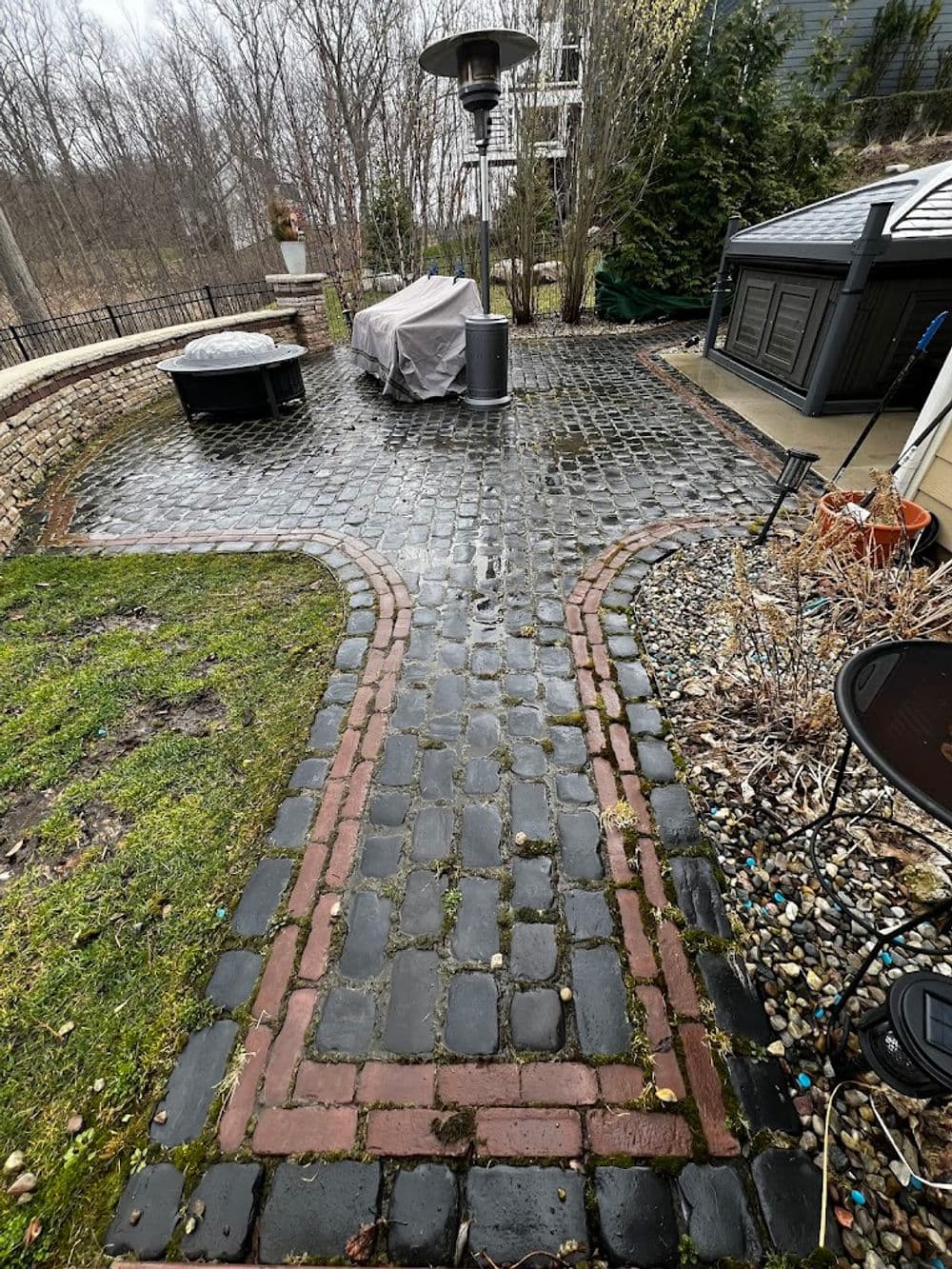 Patio with cobblestone path, gazebo covered, and outdoor heater, surrounded by greenery.