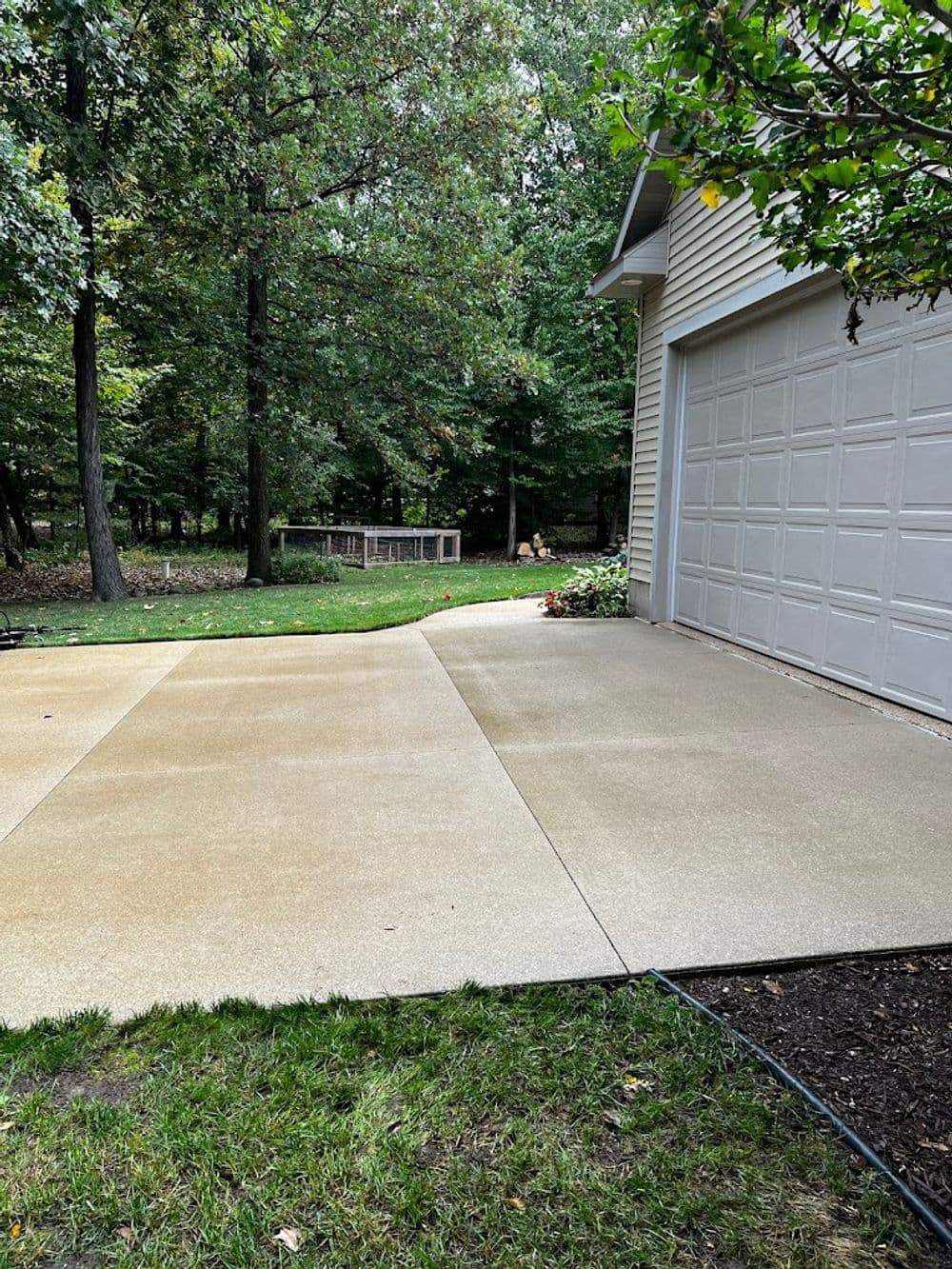 Newly paved driveway with smooth cement surface, surrounded by trees and a garage.