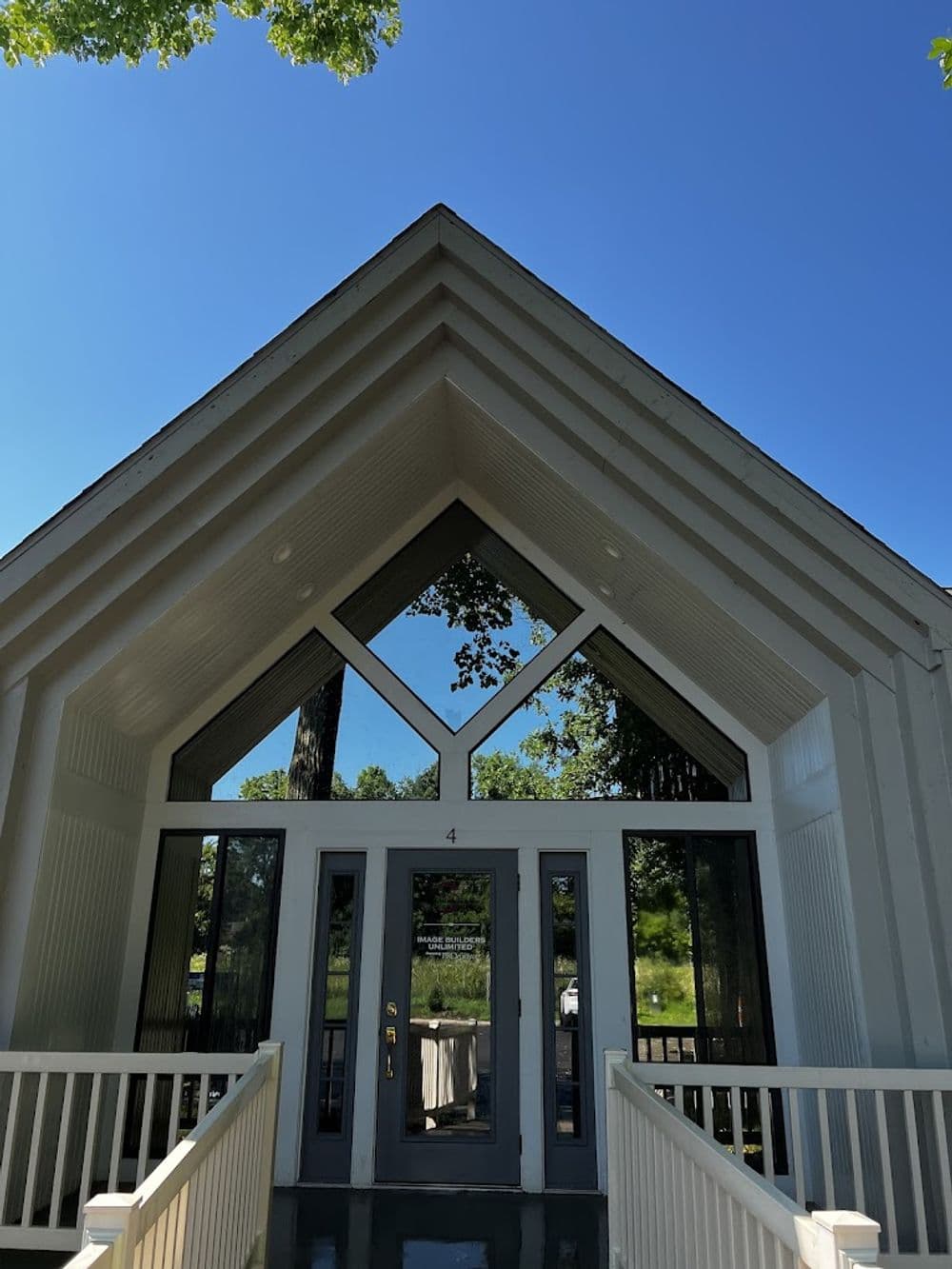 Modern white chapel with triangular roof and large glass entrance under a clear blue sky.