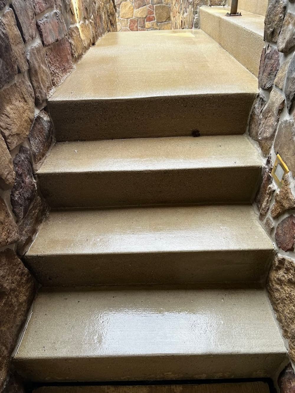 Wet concrete stairs leading up, surrounded by stone walls, showing a clean, polished finish.