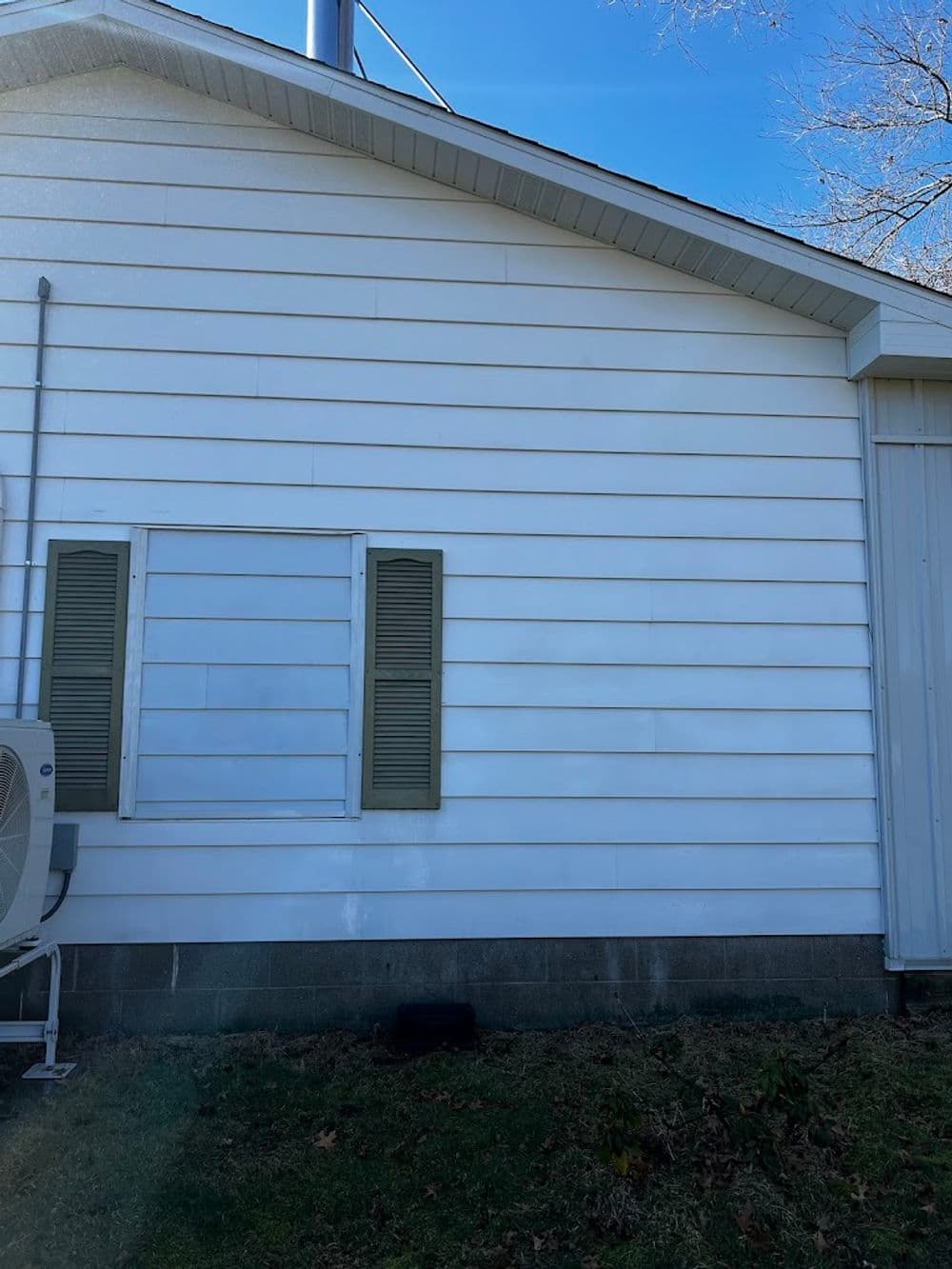 Side view of a white house with green shutters and an air conditioning unit.