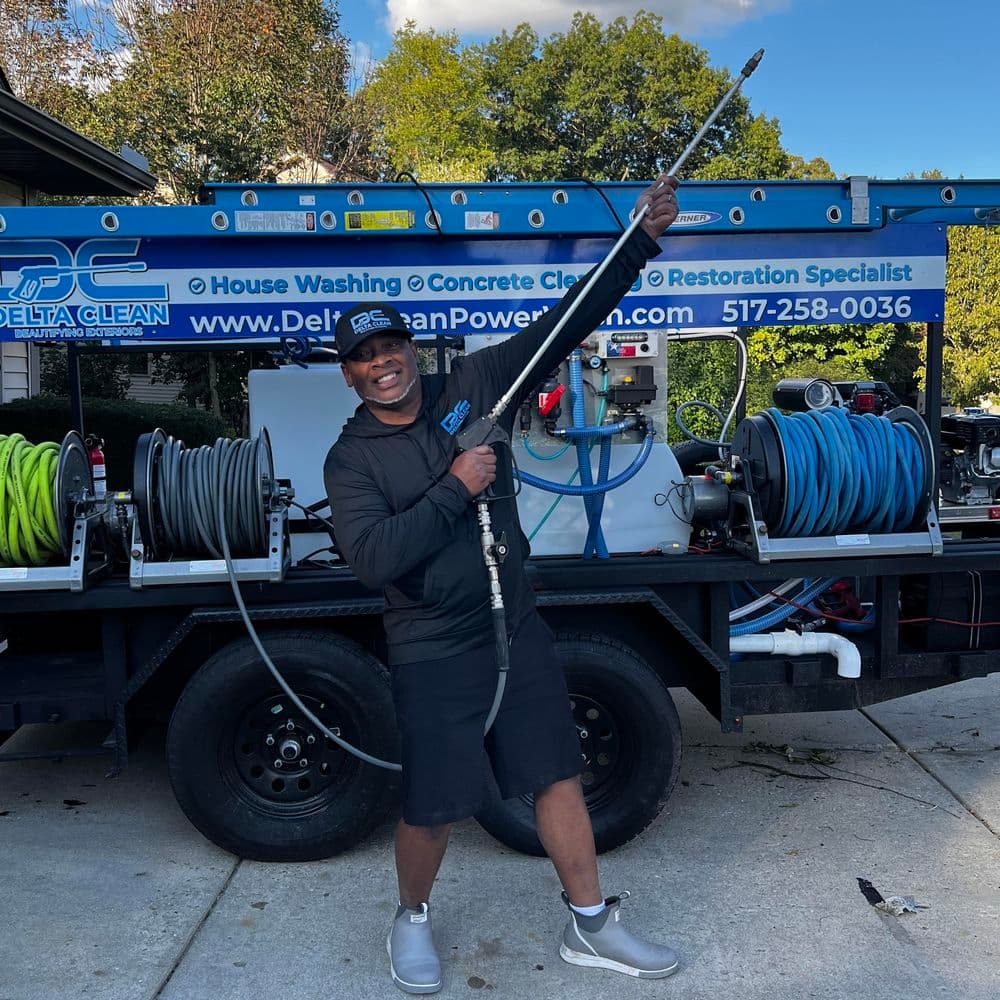 Smiling technician holding a pressure washer wand next to a truck equipped for cleaning services.