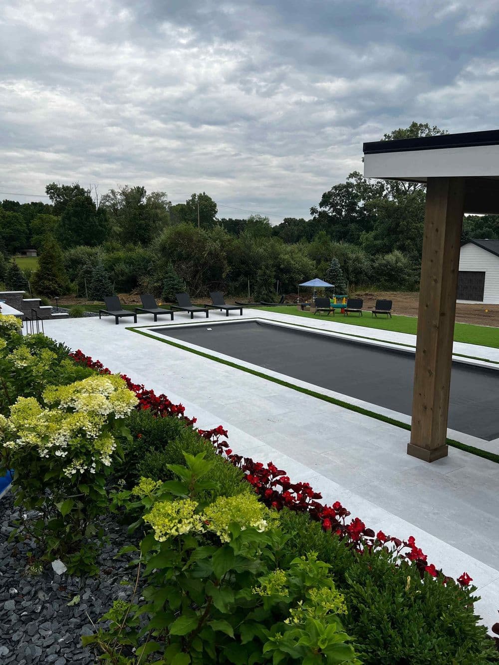 Modern outdoor pool surrounded by landscaped gardens and colorful flowers under a cloudy sky.