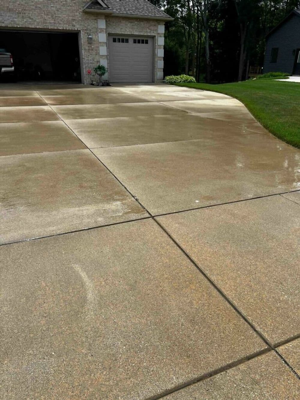 Clean, wet concrete driveway leading to a garage with a house in the background.