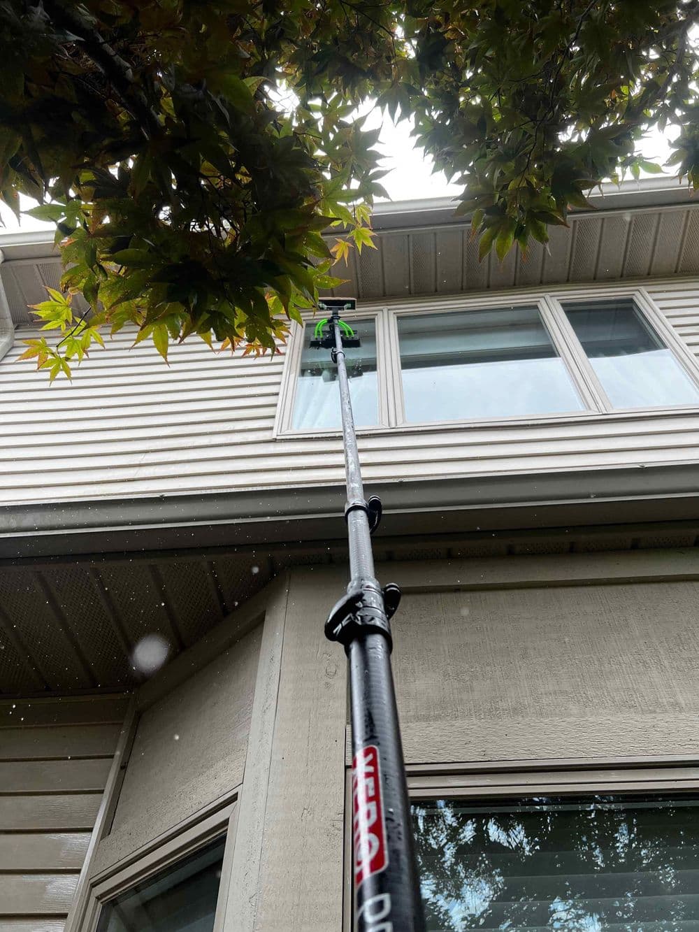 Extension pole used for cleaning windows on a two-story house under a leafy tree.