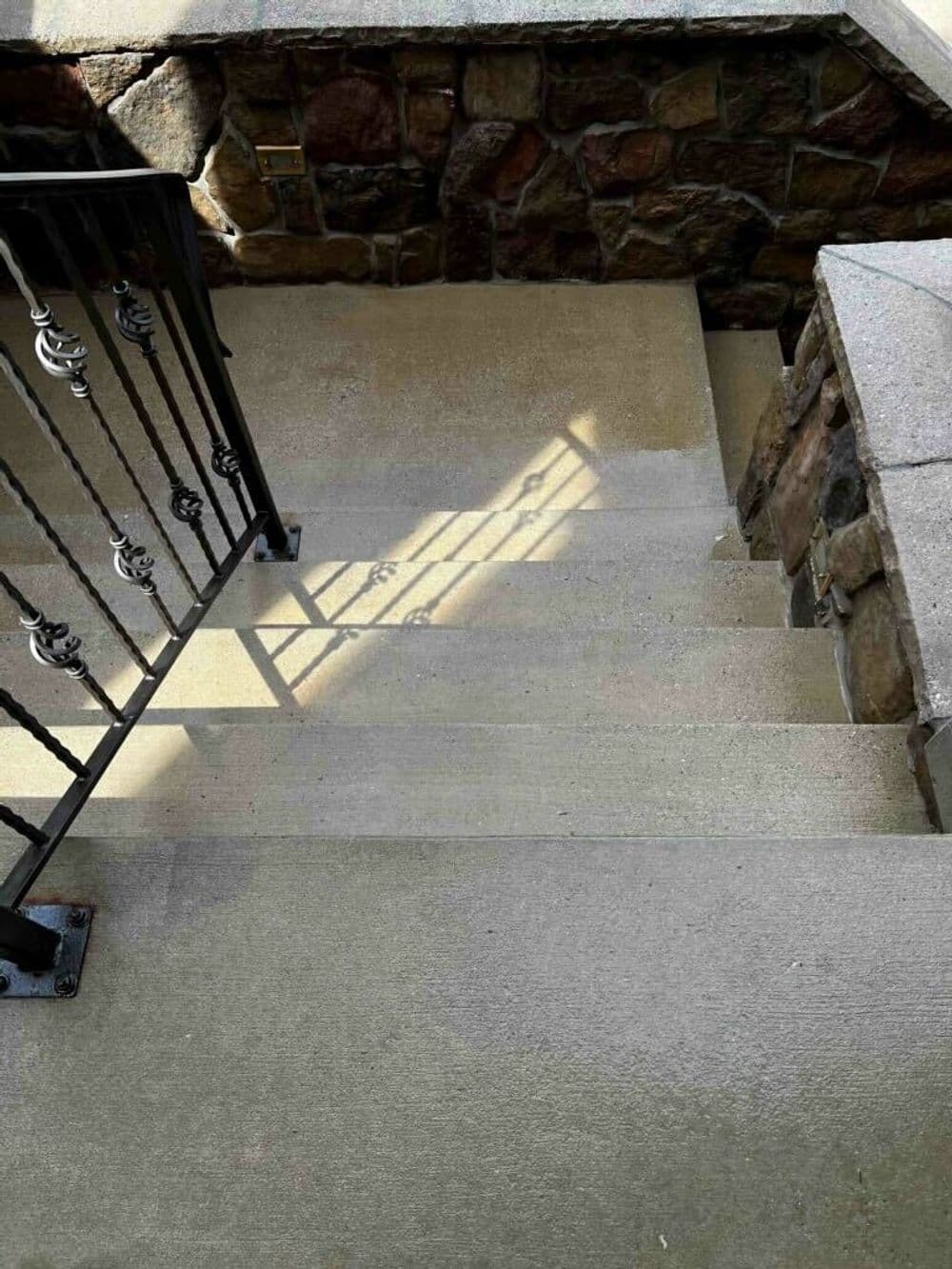 Stairs with a stone wall and metal railing, showcasing light and shadow effects.