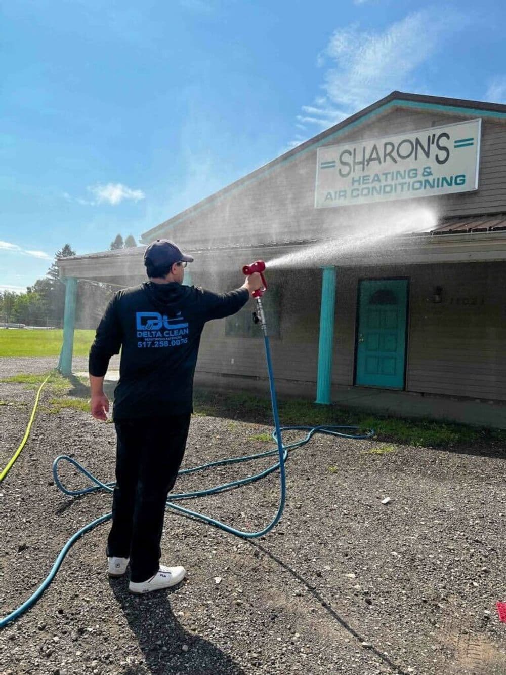 Person cleaning the exterior of Sharon's Heating and Air Conditioning building with a pressure washer.