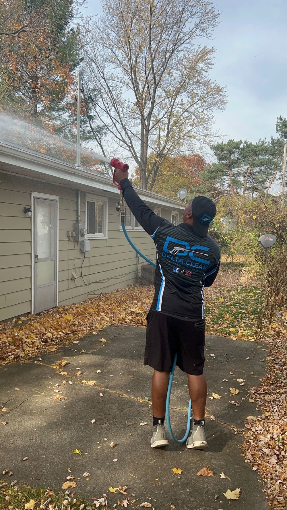 Person using a pressure washer on a house gutter surrounded by autumn leaves.