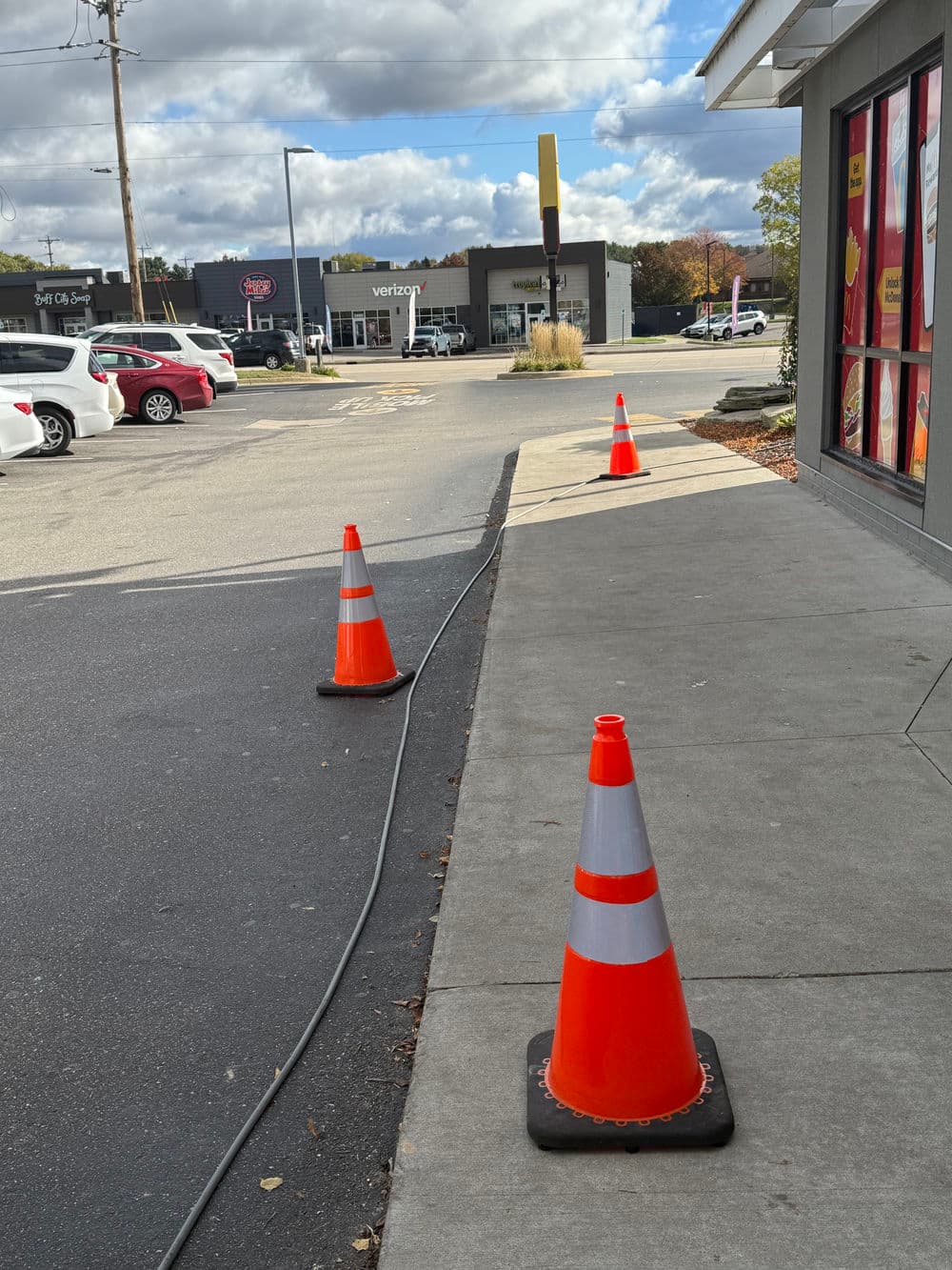 Traffic cones line the sidewalk near a fast food restaurant and shopping center.